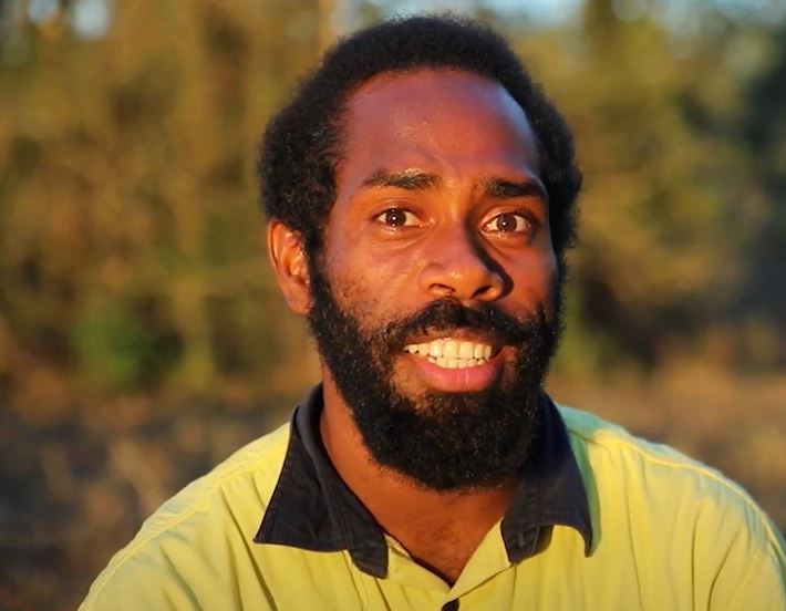 A ni-Vanuatu man wearing a yellow hi-vis shirt smiling at the camera.