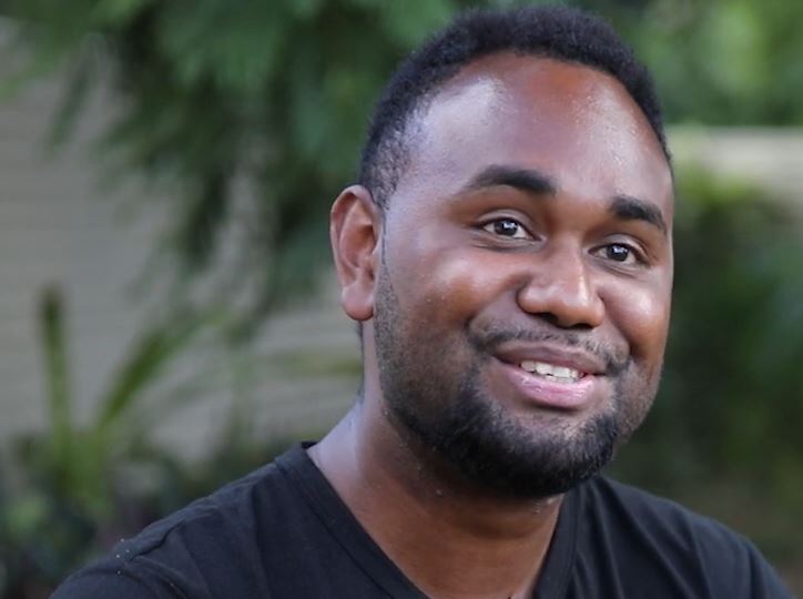 A man wearing a black shirt smiles to the camera.