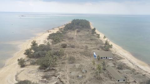 Aerial view of the aftermath of the volcano in Tonga showing houses and trees on a sandy low-lying piece of land washed out and covered in a layer of mud.