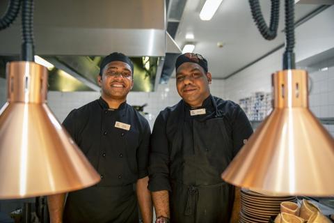 Two men standing in a commercial kitchen smiling 