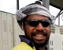 A man wearing a scarf on his head and sunglasses smiling.