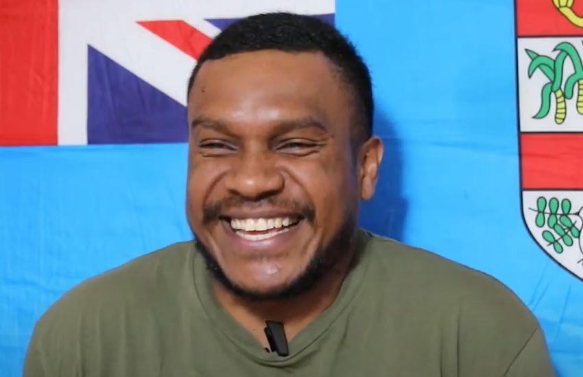 A man is laughing in front of a Fijian flag.